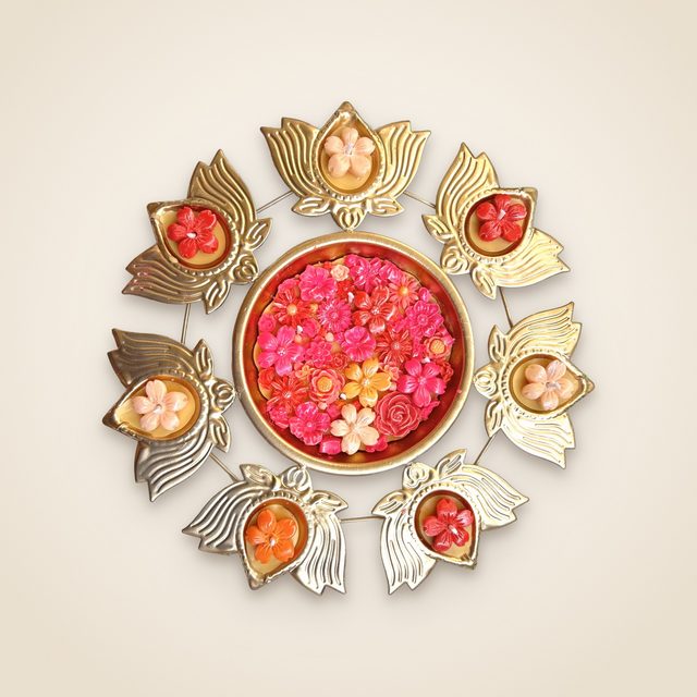 DH-01: Seven lotus diyas on a gold metal stand, around an urli of pink and red blooms.