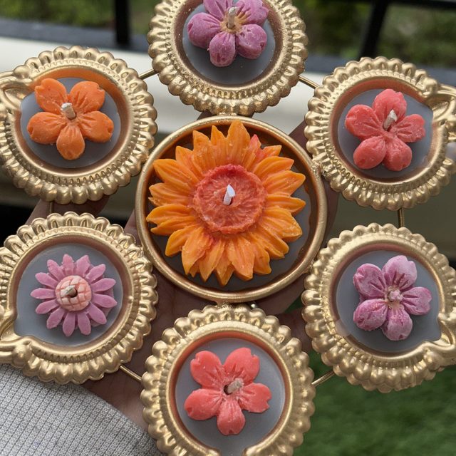 DH-03: Six flower diyas around one big orange bloom, joined in a gold metal frame.