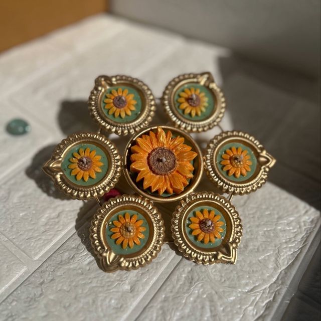 DH-04: Six sunflower diyas around one big sunflower, joined in a gold metal frame, on a white table.