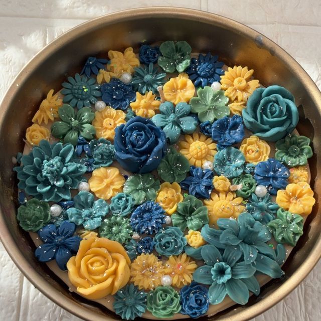DH-05: An antique-gold metal urli full of blue, teal and yellow flowers, the full bowl from above.