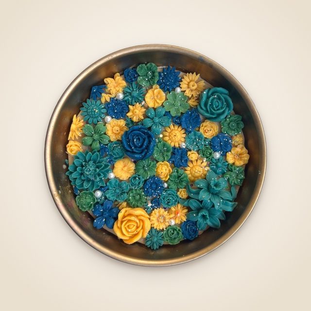 DH-05: An antique-gold metal urli full of blue, teal and yellow flowers.