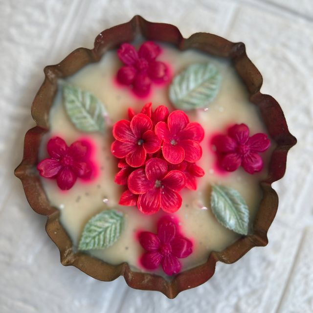 DH-07: Red and pink blooms with leaves on ivory wax, in a scalloped metal tray, on a white table.