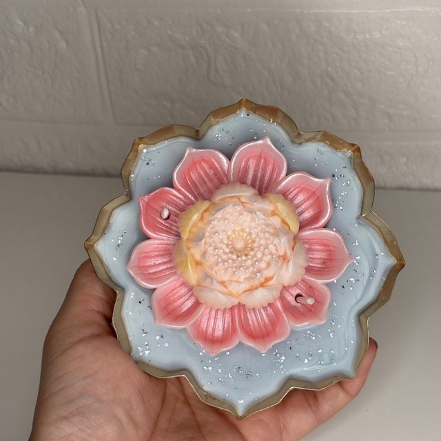DH-08: A pink lotus on blue wax, in a lotus-shaped metal tray, held in a hand, to show its size.