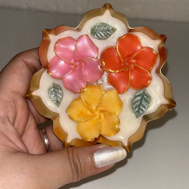 DH-09: Three plumeria blooms in a scalloped gold metal tray, held in a hand, to show its size.