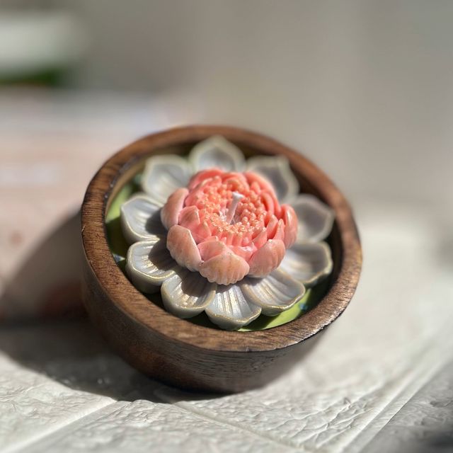 DH-13: A peach lotus on green wax, in a round wooden bowl, from the side.