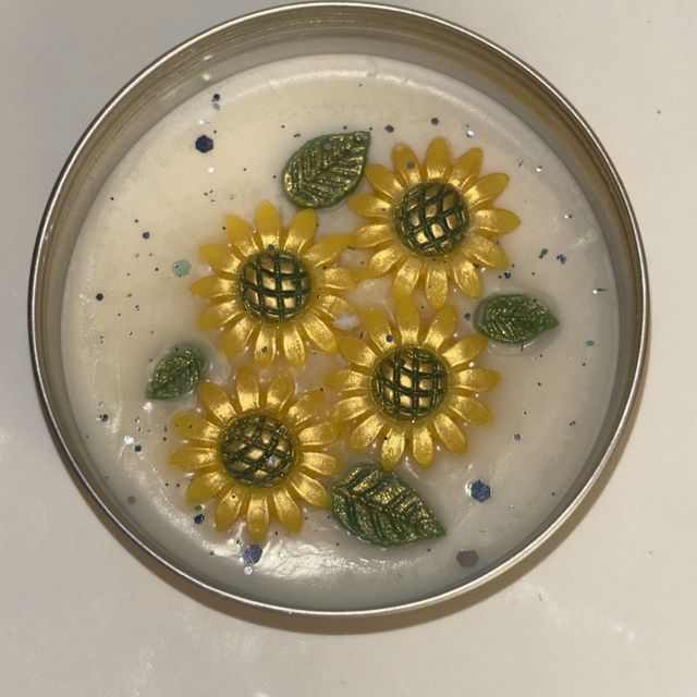 DH-15: Four sunflowers on ivory wax, in a metal tin, from above.